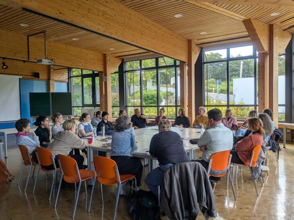 Ein Treffen im Mehrzweckraum einer Gruppe Fachschüler*Innen, Lehrer*Innen der Fachschule für Keramik in Höhr-Grenzhausen und ortsansässiger Keramiker*Innen 
